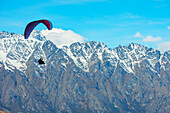  Paragliding in der Nähe der schneebedeckten Remarkables-Bergkette, Queenstown, Südinsel, Neuseeland 
