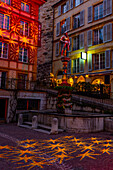 Fountain with Statue and an Illuminated House and Illuminated Stars on the Cobblestone Street in Old Town in a Dusk in City of Neuchatel, Canton Neuchatel, Switzerland.