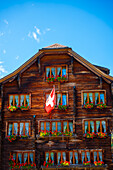 Beautiful Old Town with a Wood House with Flower and Swiss Flag in a Sunny Summer Day in Andermatt, Uri, Switzerland.