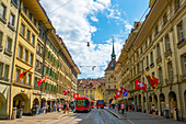 Beautiful Old City Street with Old Building and Flags and a Tram in a Sunny Summer Day in City of Bern, Canton Bern, Switzerland.