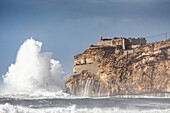  View of the cliffs and the Farol de Nazare lighthouse. Very high waves crash against the coast, Leiria, Portugal 