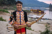  Young man with traditional bamboo harmonica, behind him the boutique river cruise ship Anouvong (Heritage Line), anchored on a sandbank on the upper Mekong, Bhan Khok Aek, Hongsa, Sainyabuli, Laos, Asia 