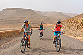 Mountain bikers with electric assistance on the road from Zagora to the south (N 9), Draa River valley, Province of Zagora, Region Draa-Tafilalet, Morocco, North West Africa