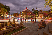 People sit on the steps at Jalan Raya Ubud street illuminated at dusk. Ubud, Bali, Indonesia.