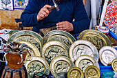  Craftsmen working on brass plates with carved scenes and figures at the market in the Medina in Hammamet, Tunisia 