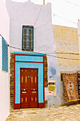  Traditional house with colorful wooden door with Arabic carvings and woven carpets for sale on the house wall in Hammamet, Tunisia 