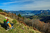 Zwei Personen sitzen auf Aussichtsbank und blicken auf Wolfgangsee und Salzkammergutberge, Zwölferhorn, Salzkammergut, Salzburg, Österreich