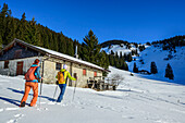 Mann und Frau beim Winterwandern, Almgebäude im Hintergrund, Dürrnbachhorn, Reit im Winkl, Chiemgauer Alpen, Oberbayern, Bayern, Deutschland