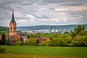  View of Kunitz with church in the foreground and the city of Jena with the Jentower in the background, surrounded by green fields and hills under a cloudy sky, Kunitz, Thuringia, Germany 