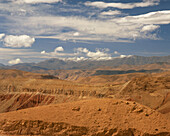 Snow covered mountains of the High Atlas in the distance with a desert track weaving through the barren foothills towards the Valley of the Roses, near Boumalne Dades, Morocco.
