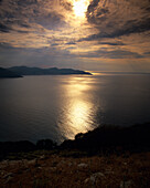 The sun sets behind clouds over Myrtou bay on the west coast of Kefalonia