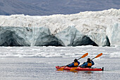 Zwei Kajakfahrer paddeln mit ihrem Boot in der Nähe von Eis und der Vorderseite eines Gletschers bei Waltershausen, Arktisches Grönland, Grönland, Europa