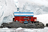  A member of the Argentine Brown Base sits in front of the wooden building with an image of the country&#39;s flag on the roof, Paradise Bay, Antarctic Peninsula, Antarctica 
