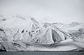  A barren, monochrome scene of snow-capped mountains in the caldera opposite Whalers Bay, Deception Island, South Shetland Islands, Antarctica 