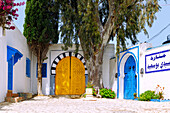 reich verzierte gelbe und blaue Holztür und blühende Bougainvillea beim Leuchtturm in der (Medina) Altstadt von Sidi Bou Said, Tunesien