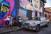  Five men pose in front of a colorful mural in the Bellavista district with a damaged pickup truck parked on the street, Santiago de Chile, Santiago, Chile, South America 