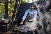  Smiling chef prepares delicious steamed seafood during a barbecue on the terrace of Patagonia Camp, Torres del Paine, Magallanes y de la Antartica Chilena, Patagonia, Chile, South America 