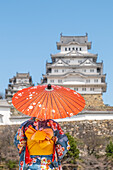 Woman wearing a traditional Japanese kimono with umbrella in front of the Himeji castle (White Heron Castle), Japan.