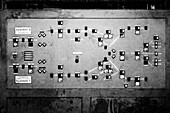 A vintage control panel with numerous switches and indicators, showcasing a complex network of systems. The panel is weathered and has a monochrome aesthetic, emphasizing its industrial design.