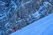  Two people on ski touring ascend in front of rock faces, Winkelkar, Kaiser Mountains, Tyrol, Austria 