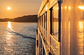 Spiegelung in Fenstern an der Seite des Boutique-Flusskreuzfahrtschiffs MS Thurgau Saxonia (Thurgau Travel) im Peenestrom bei Sonnenaufgang, Wolgast, Mecklenburg-Vorpommern, Deutschland, Europa