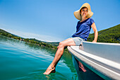 Young woman sitting at the prow of a small boat powered with electric motor on the  natural Lake of Aiguebelette, department of Savoie, Rhone-Alpes region, France, Europe