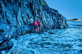  Two women hiking on a rock platform above the ocean surf, Wild Coast Trail, Wild Coast, Eastern Cape, South Africa 