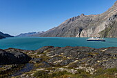 Expeditionskreuzfahrtschiff World Voyager (Atlas Ocean Voyages) mit Felsen im Vordergrund und Bergen dahinter, Sermillinnguaq Fjord, Queqatta, Grönland, Europa