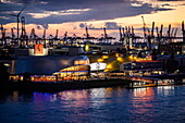  Illuminated musical theaters &quot;MJ The Michael Jackson Musical&quot; and &quot;The Lion Queen&quot; on the Elbe River with cranes in the background at sunset, Hamburg, Germany, Europe 
