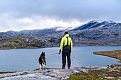  Norway, Nordland, Gjerdalen, Sørfold, man with dog, mountain landscape with glacier and Lake Jierddajávrre 