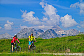  Man and woman mountain biking towards the Gotzenalm, Steinernes Meer in the background, Berchtesgaden National Park, Berchtesgaden Alps, Berchtesgaden, Upper Bavaria, Bavaria, Germany 