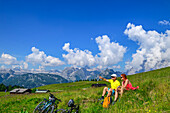  A man and woman take a break while mountain biking, with the Steinernes Meer mountain range in the background, Gotzenalm, Berchtesgaden National Park, Berchtesgaden Alps, Berchtesgaden, Upper Bavaria, Bavaria, Germany 
