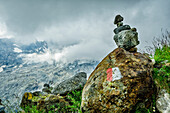  Trail marker and cairn against a cloudy backdrop, Valmalenco, Alta via della Valmalenco, Bernina Alps, Lombardy, Italy 
