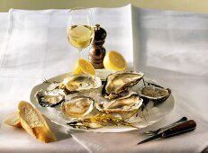Oysters & lemon on ice on plate, wine glass on table