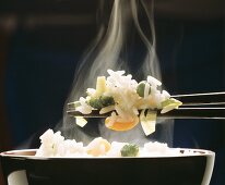 Dampfender Reis mit Gemüse auf Stäbchen über Reisschale