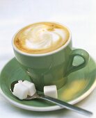 Cappuccino in green cup with spoon and sugar cubes
