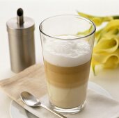 A glass of latte macchiato in front of a sugar sifter