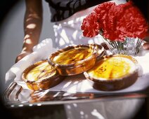 Hands holding tray with crema catalana & carnations