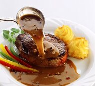 Pouring pepper sauce over beef steak