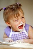 Kleines lachendes Mädchen beim Backen mit Mehl im Gesicht