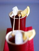 Zwei Becher Früchtetee mit Zitronenschnitzen, Kandissticks