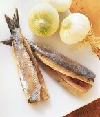 Two herrings without heads with onions on chopping board