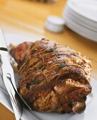 Roast leg of lamb with rosemary on platter with cutlery