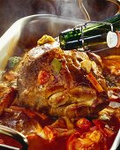 Basting roast pork & tomatoes with beer in roasting dish