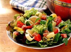 Salad leaves with ham on plate, sieve with tomatoes beside it
