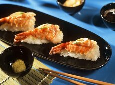 Nigiri with shrimp tails on black platter; chopsticks