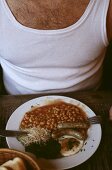 Man in vest eating beans with sausage and fried egg