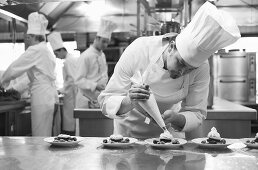 Chef piping cream onto berry desserts