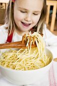 Girl lifting spaghetti out of bowl with spaghetti server