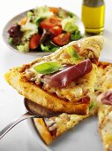 Slice of pizza with ham on server, salad in background